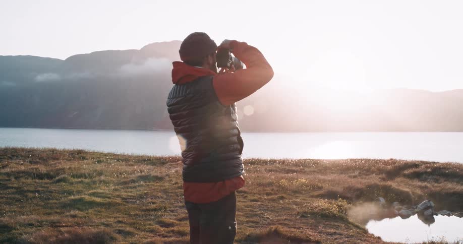 A man taking a photo of a mountain range beyond a lake