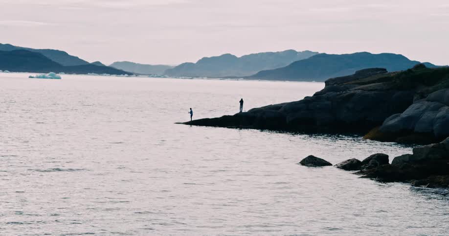 Two people in silhouette fish on the coast at dusk