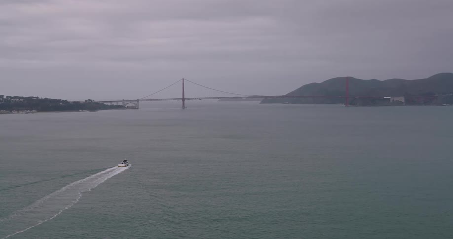 A boat drives across a vast lake approaching a bridge connecting mountains