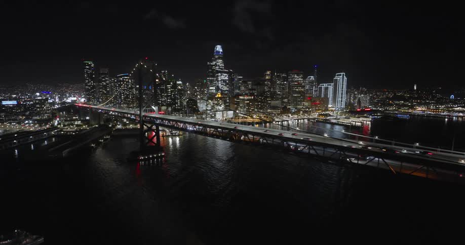 Aerial view of traffic over a bridge next to a waterfront city at night