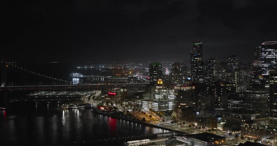 Aerial panoramic of the downtown city skyline by the bay lit up at night with a black clouded sky and thin fog
