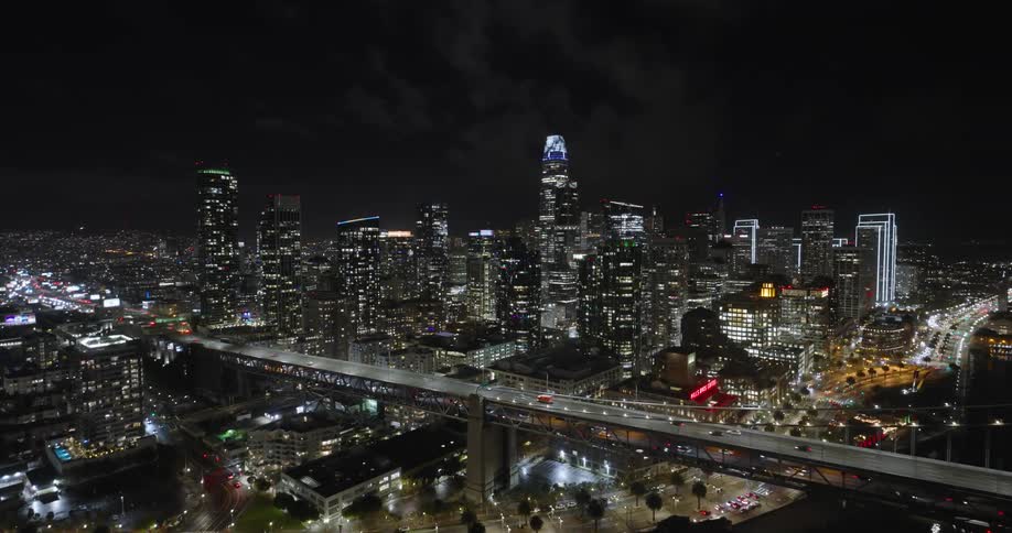 Aerial of freeway bridge city skyline at night dotted with white lights and a black sky with thin smoke clouds