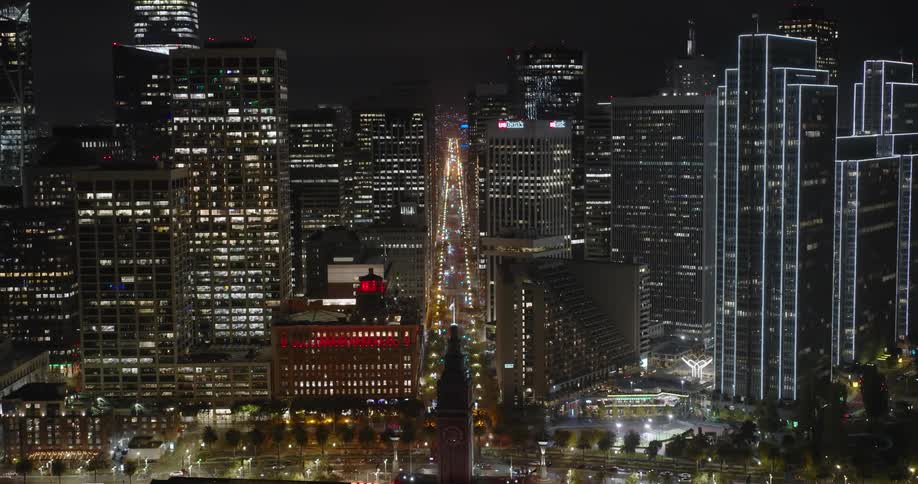 Lights on metropolitan buildings and towers glow in the darkness as traffic moves on the streets