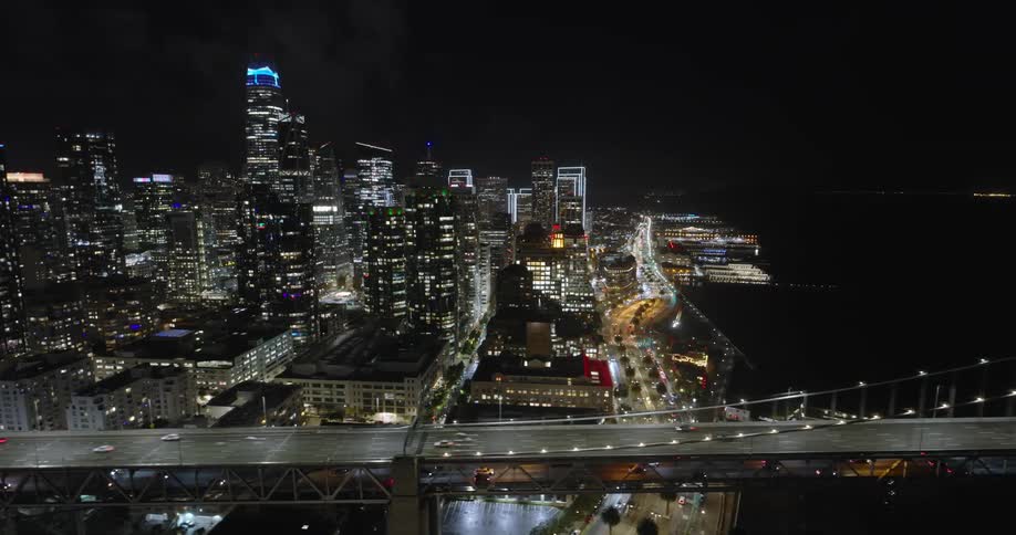 Landscape of buildings and moving vehicles on a metropolitan bridge at night