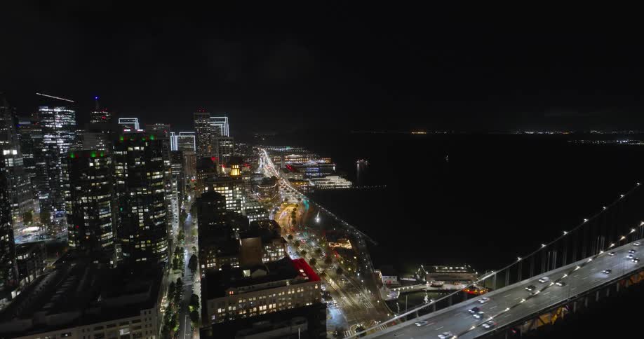 Aerial panorama of a metropolis with skyscrapers at night by the sea and with a bridge with vehicles in motion