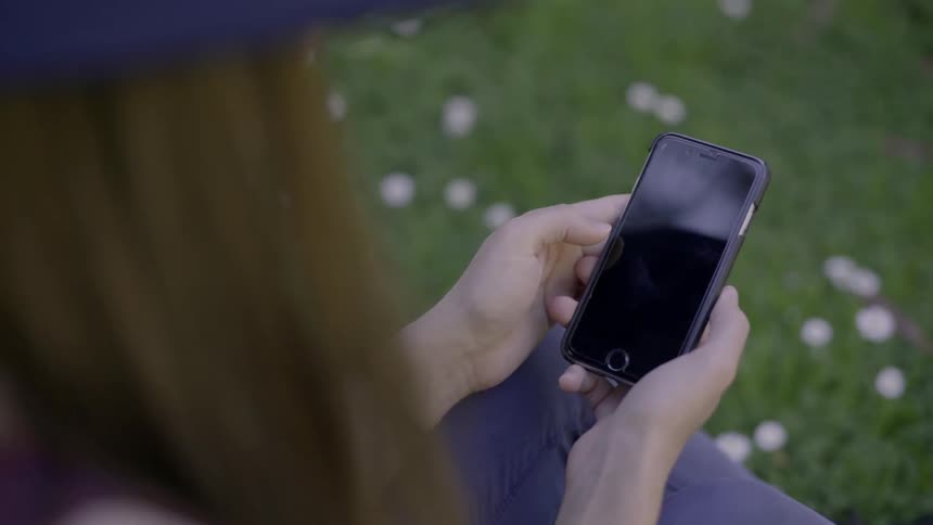A woman scrolls on her phone while sitting in the grass
