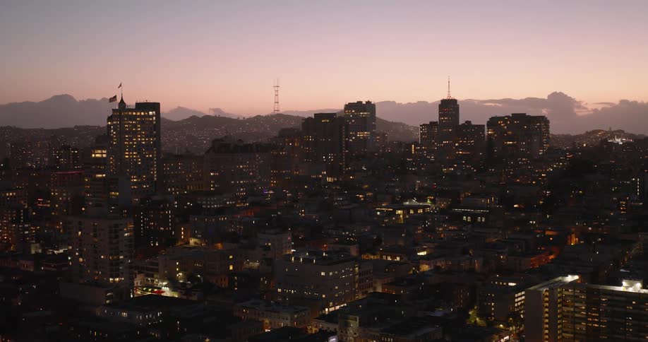 Window lights twinkle across a city skyline with a smoggy purplepink sky at dusk