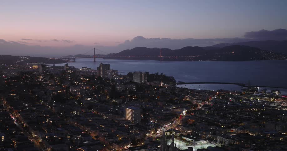 A lit up city sits in front of a river at dusk