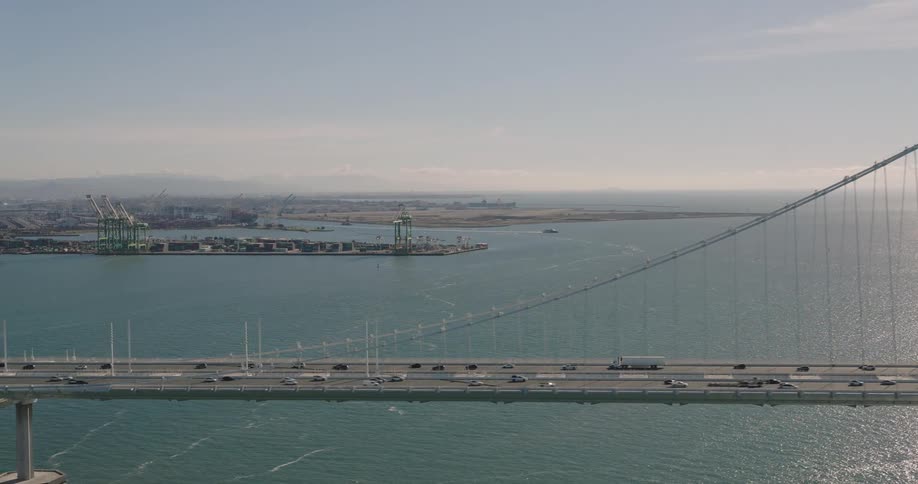 Traffic crosses suspension bridge over water with loading dock in the background