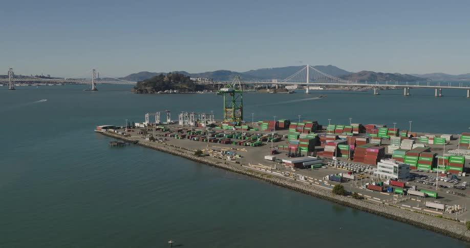 Aerial of loading docks across water from mountains and city skyscrapers