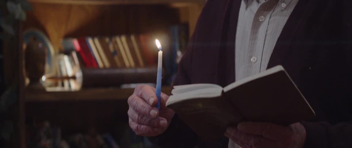 A clip on an elderly man holding a bible and candle praying