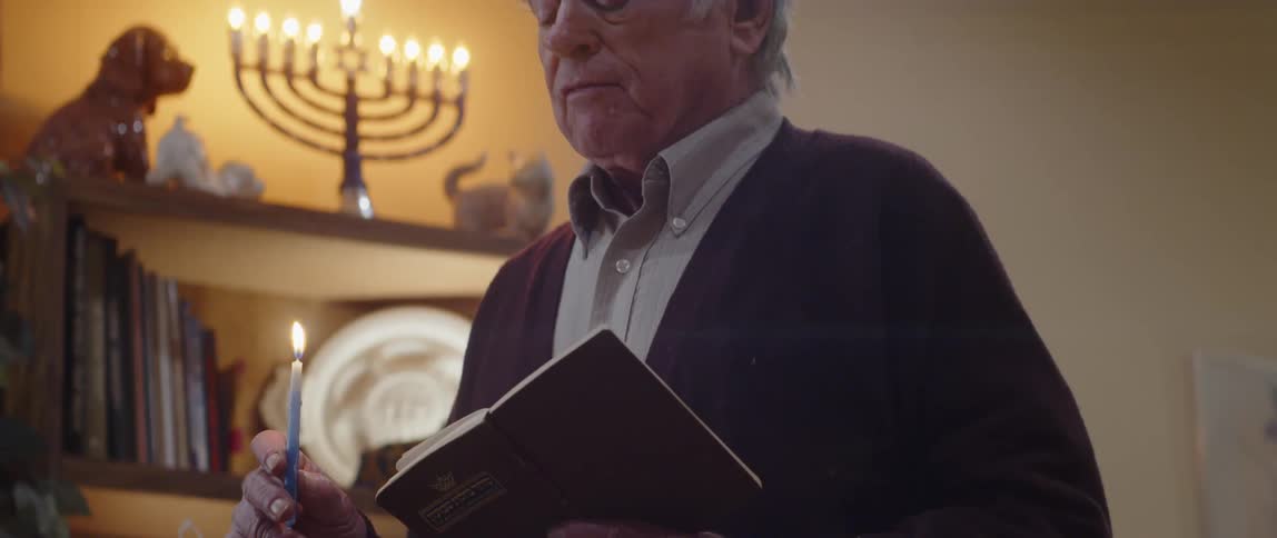 An elderly man holding a candle while reading a book
