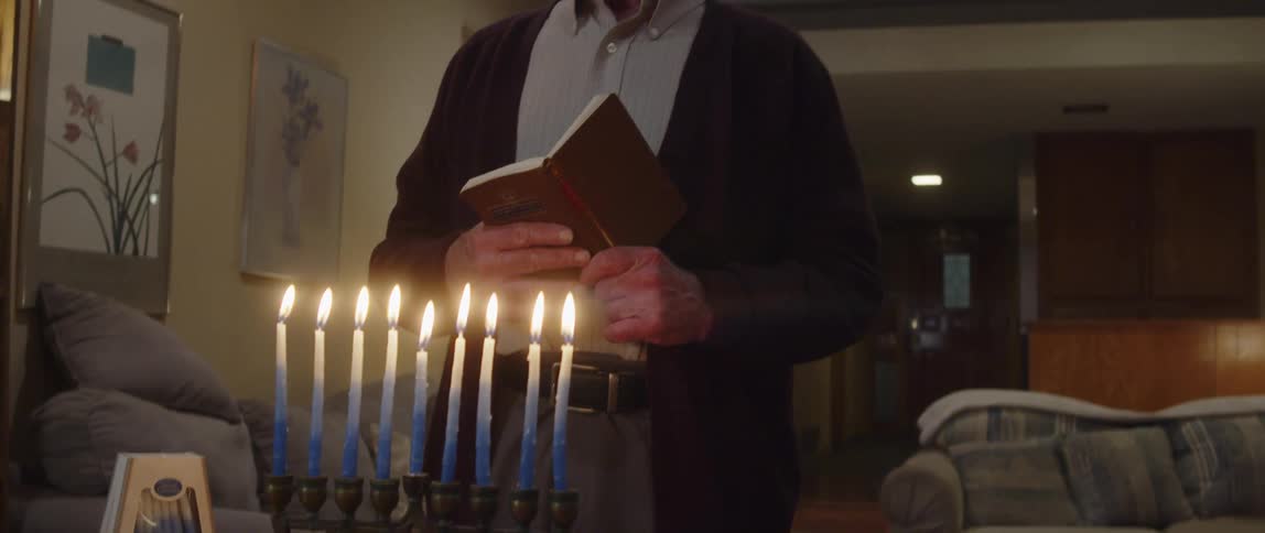 Jewish man praying in front of a menorah at home