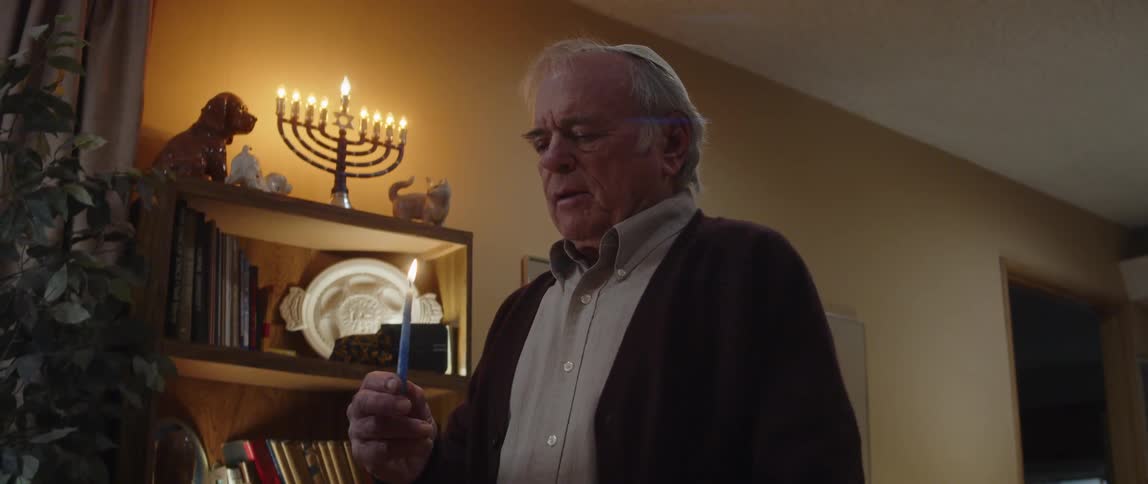 Jewish man praying in front of a menorah at home