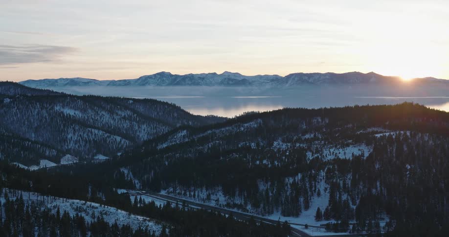 Aerial panorama of a mountain range with conifers a lake and a morning sun