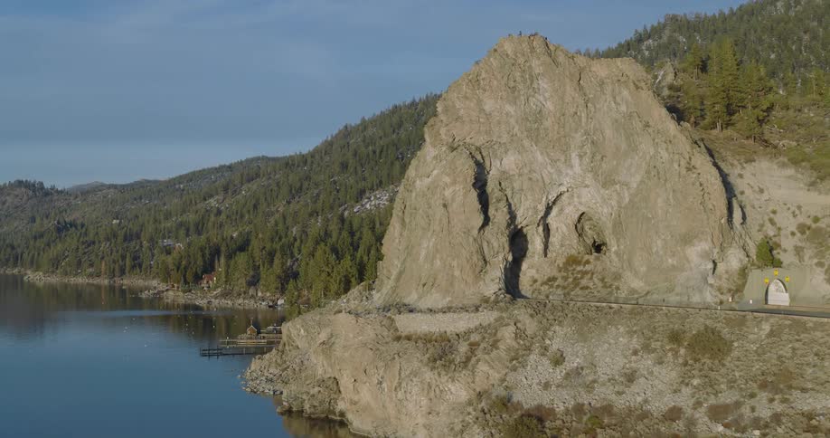 A coastal region with tall rocks and a tunnel going through them and there is a lake next to it