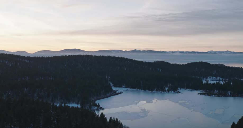 Aerial of a frozen lake surrounded by a snowy forest