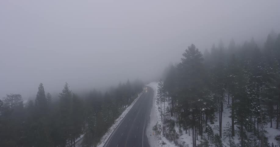 Aerial along a highway along a tree covered mountain slope covered in a thickening fog right before nightfall