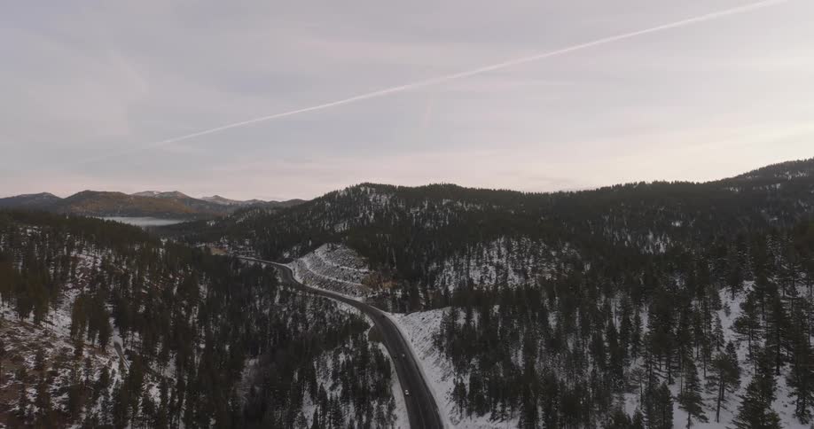 Cars drive on the highway past the hills and trees