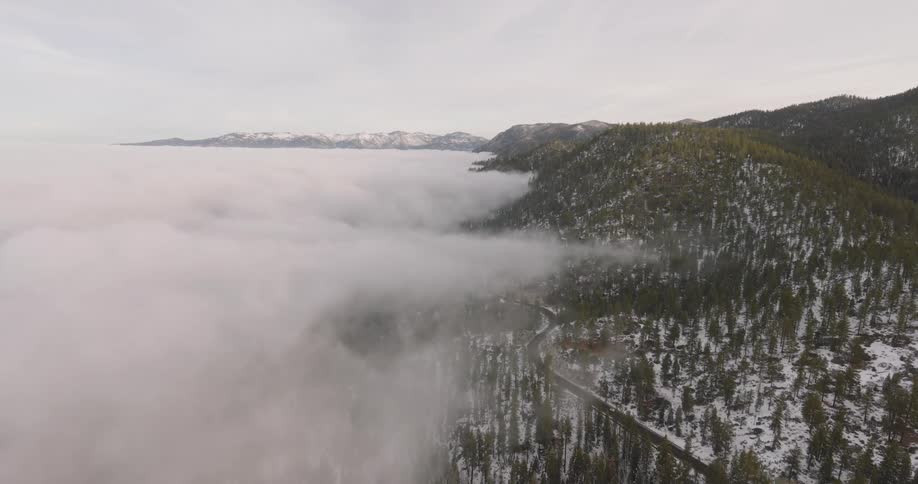 Aerial view over a tree and snow covered ridge slope partially covered in fog