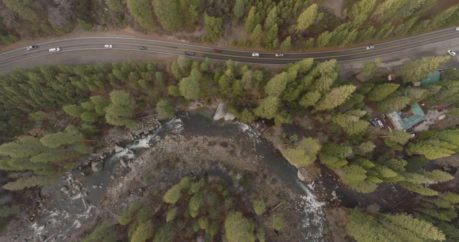 Aerial top view of cars driving on a curved highway and river surrounded by tall pine tree forest during on a dull day