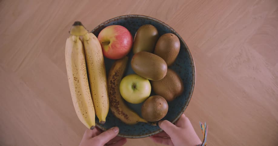 A bowl with bananas an apple and kiwis is placed onto a wood grain table
