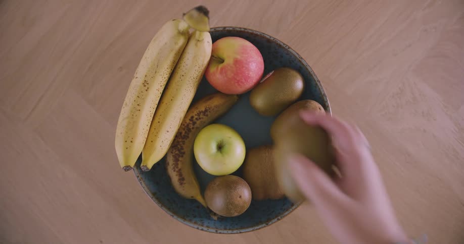 Closeup of a womans hands picking up a kiwi from a table