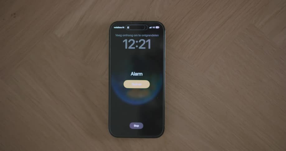 A cell phone sits on a table as the alarm goes off a persons hand is seen picking it up