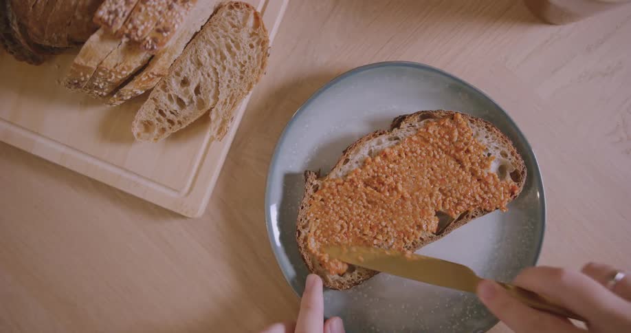 A person uses a knife to spread jam over a slice of bread