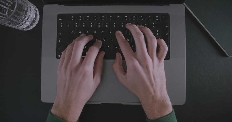 A man sits at a desk while typing quickly on a laptop keyboard