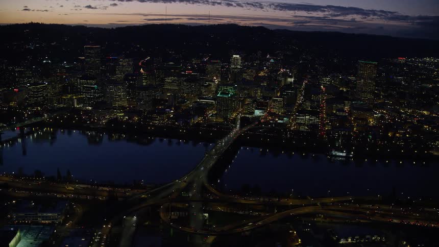 Aerial panorama of a nighttime metropolis with a central lake under a purple dusk sky