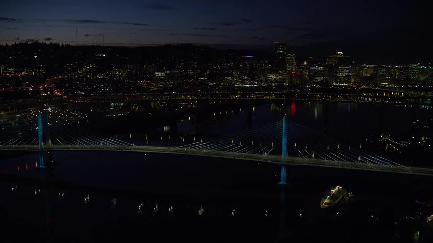 Traffic crosses bridges over water at night with downtown skyline in the background