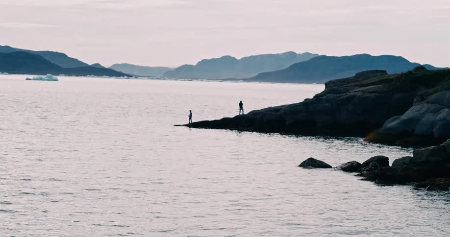 Two people on top of rocks fishing by the sea