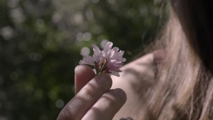 A woman holds a flower bud and twirls it on a sunny day