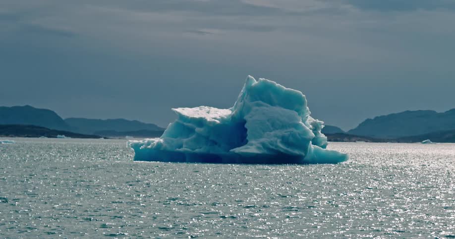 The sun shines upon a melting iceberg floating off the arctic coast
