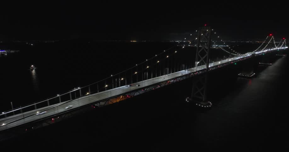 Panorama of a massive bridge over the sea at night with vehicles moving
