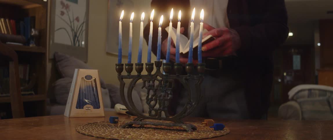 Jewish man prays in front of a hanukkah menorah at home