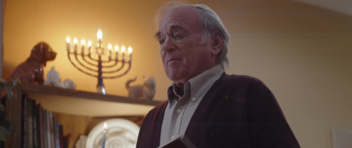 Jewish man praying in front of a menorah at home