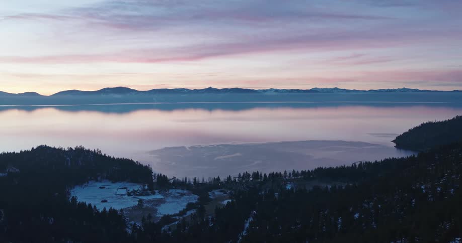 Aerial panorama of mountains facing a reflective sea under a purple morning sky