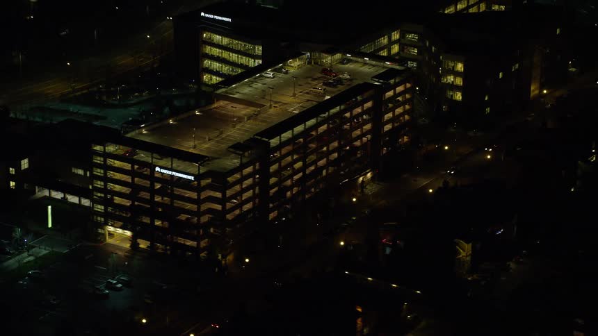 Traffic moves along city streets passing block of parking garages at night