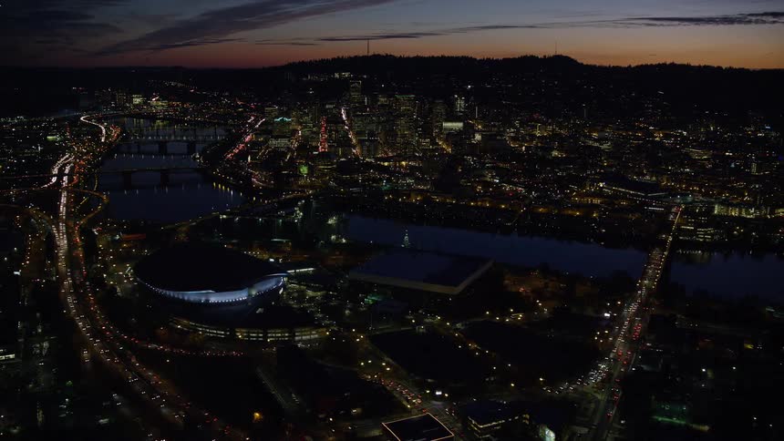 Aerial view shows a vast city lit up at night under a beautiful sunset