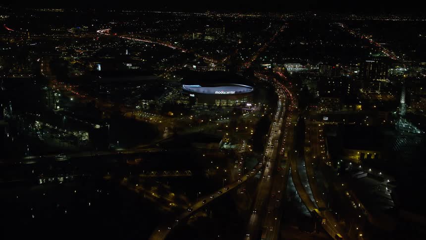 Aerial panorama of a metropolis with nighttime traffic on the streets and a covered stadium