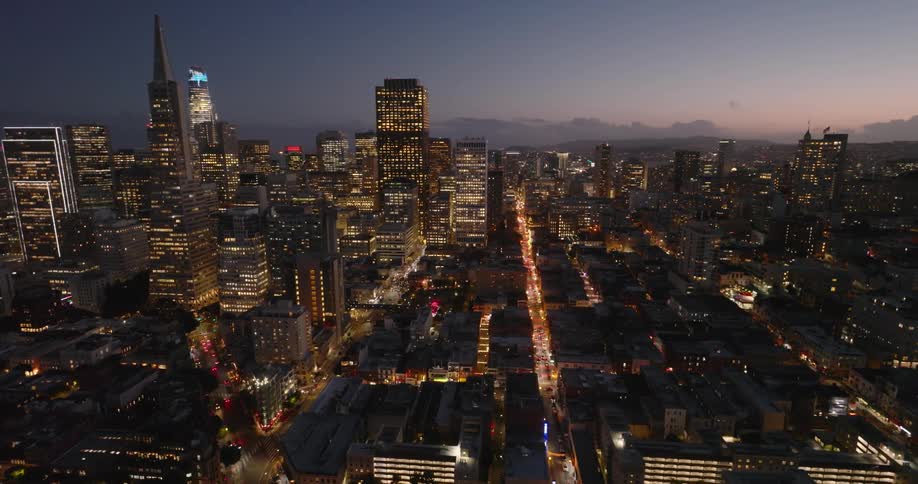 Lights on metropolitan buildings and towers glow in the darkness as traffic moves on the streets