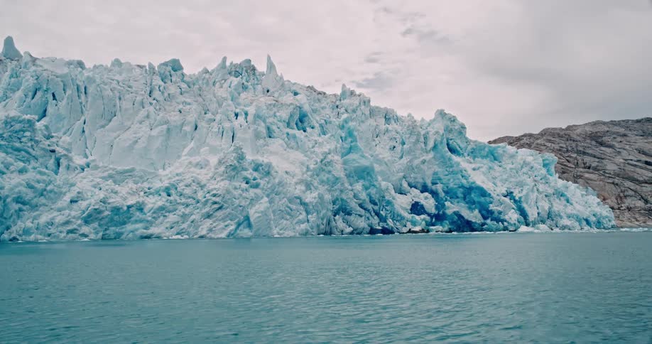 Large glacial ice borders mountainous shore on an overcast day