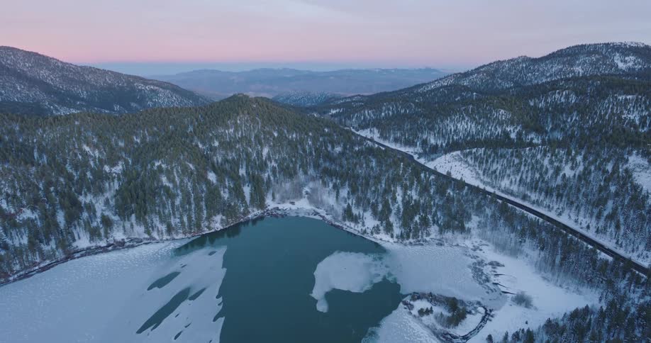 Lake covered almost completely in ice sits in front of snowcovered mountains