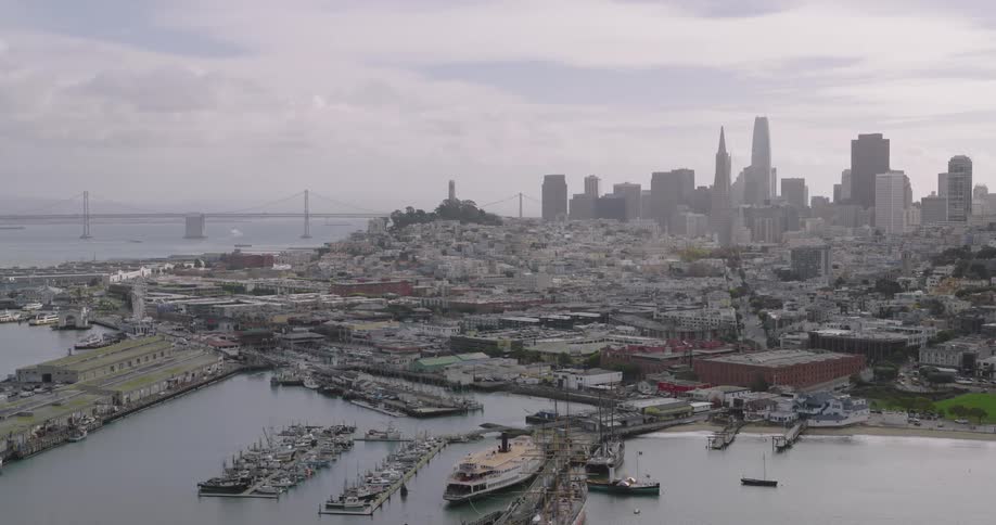 Ferryboat and sailing boat sit at dock near marina with city skyline in the background on a foggy day