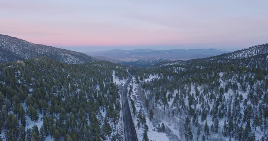 Central road amidst snowy mountains and conifers under a purple dawn sky