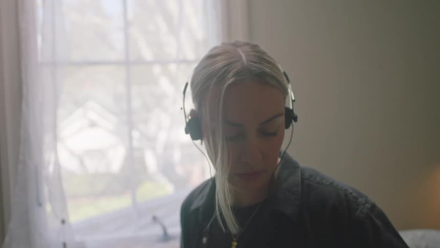 A blonde woman wearing a gray shirt listens to music with headphones in a room