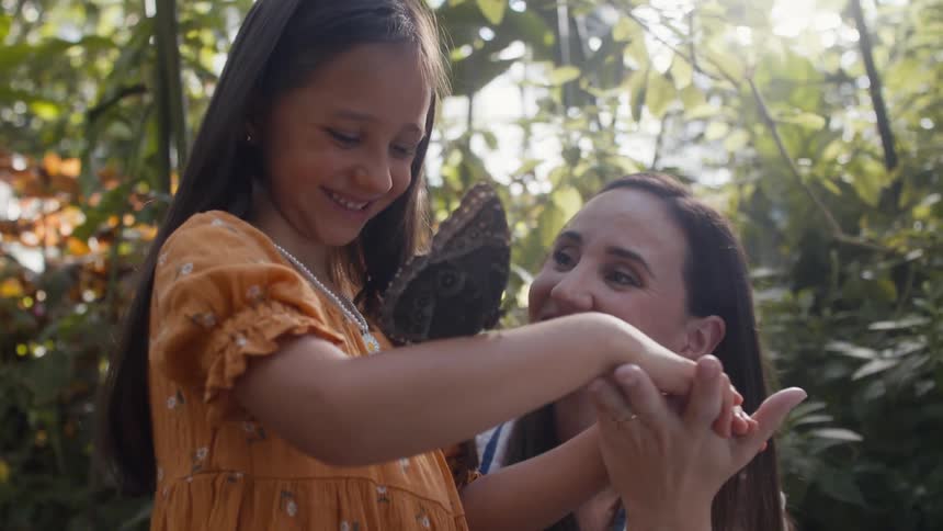 A mother and daughter look at a butterfly
