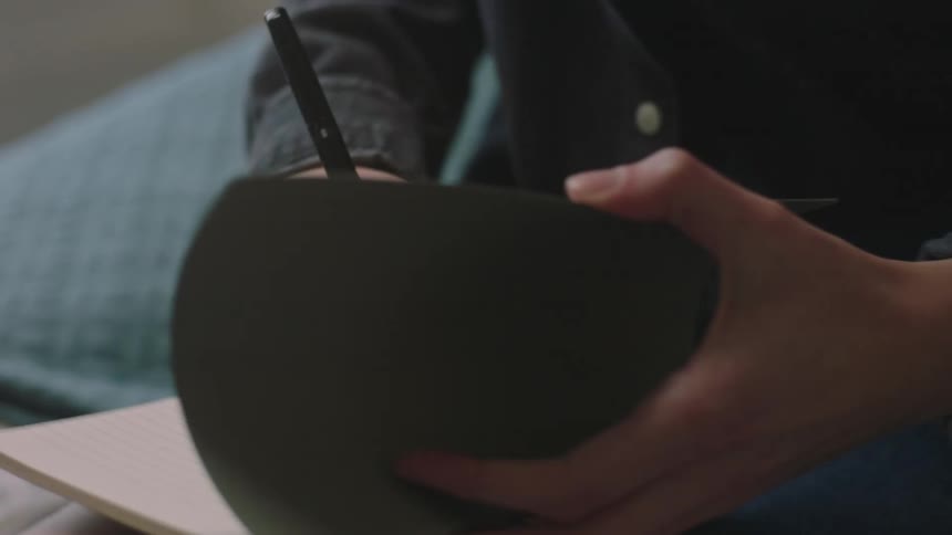 Closeup of a womans hands placing a tape in a music player and writing something in a notebook